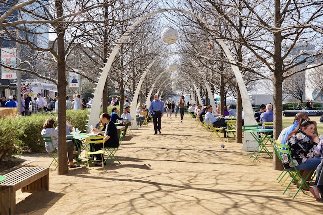 People lunching beside and walking on Klyde Warren Park walkway.